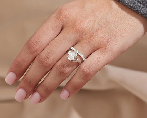 Close-up of a hand with soft pink manicure wearing a pear-shaped diamond engagement ring paired with a pavé diamond wedding band.