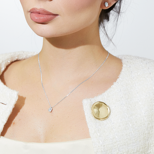 Woman wearing a textured cream jacket with a large gold button, styled with a delicate diamond pendant necklace and matching diamond stud earrings.