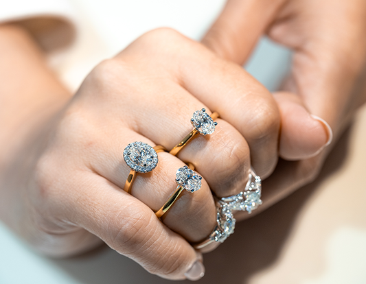 Close-up of a hand adorned with four diamond rings, including two on yellow gold bands and two on white gold or platinum bands, featuring various settings such as halo and solitaire.
