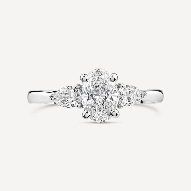 Platinum engagement ring featuring an oval-cut center diamond flanked by two pear-shaped side diamonds, set on a polished band.
