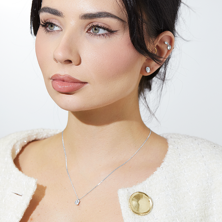 Woman wearing a textured cream jacket with a large gold button, styled with a delicate diamond pendant necklace and matching diamond stud earrings.