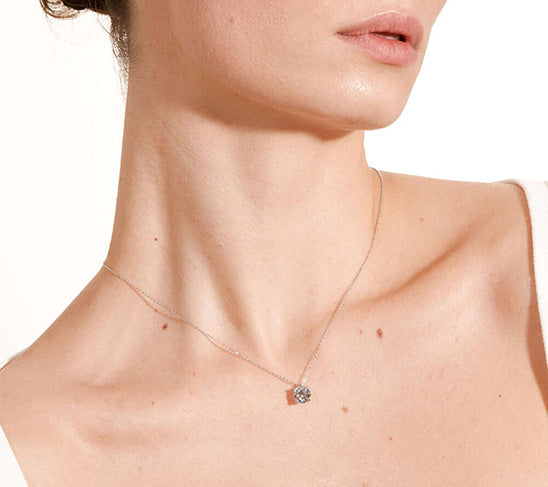 Woman wearing a delicate white gold necklace with a round diamond pendant in a halo setting.