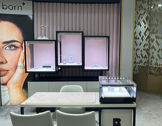Jewellery display area with "born" branding, pink-lit glass cases showcasing diamond pieces, a poster of a woman wearing jewellery, a modern counter with white chairs, and a smaller display box placed on the counter.